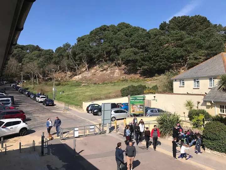 A busy scene near Bournemouth seafront with people walking and parked cars, surrounded by trees and buildings.